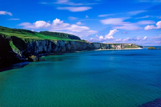 Landscape of Northern Ireland, coastline and cliff, green hills and blue sky along Causeway Coastal Route, County Antrim, United Kingdom