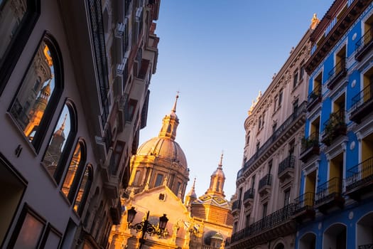 Basilica Of Our Lady Of The Pilar and historical buildings as seen from below, Zaragoza from street level, reflection of Cathedral details in glass windows on the left