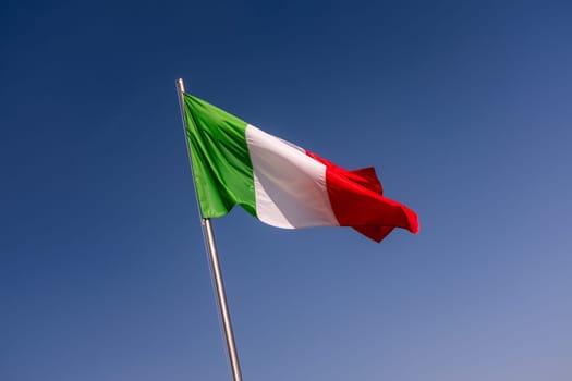 Low angle view of Italy flag waving against the clear blue sky, flagpole tilted to the left