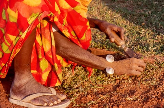 Old woman crouching beside a flowerbed and removing the growing grass on a garden path using her hands