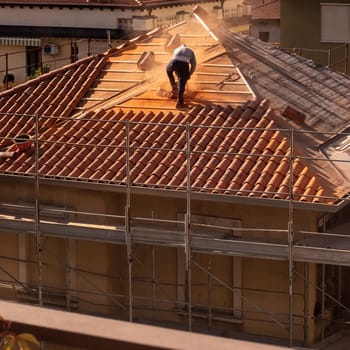 Construction worker on a renovation roof is cutting the tiles with the grinder and then places them along the ridge line