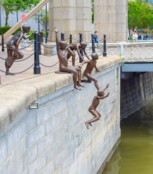SINGAPORE - FEBRUARY 16, 2017: Statue of boys jumping in water in Singapore Downtown Core district, people on bridge in background