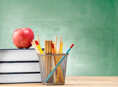 Pile of books with apple and pencils in basket container on wooden table with chalkboard background. Back to School concept
