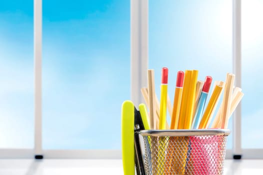 Pencils in basket container with green stapler with window glass background. Back to School concept