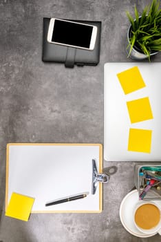 Top view of business desk with laptop, mobile phone, coffee, potted plant, notebook, notes paper, clipboard and business accessories on the office