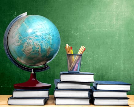 Pile of books and globe with pencils in basket container on wooden table with chalkboard background. Back to School concept