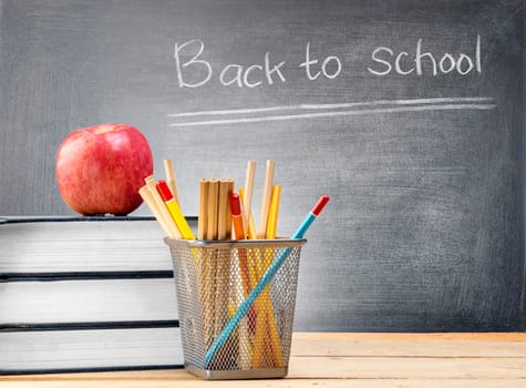 Pile of books with apple and pencils in basket container on wooden table and blackboard with Back to School message. Back to School concept