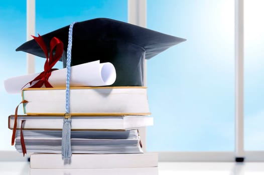 Graduation hat and diploma on pile of books on the table. Graduation concept