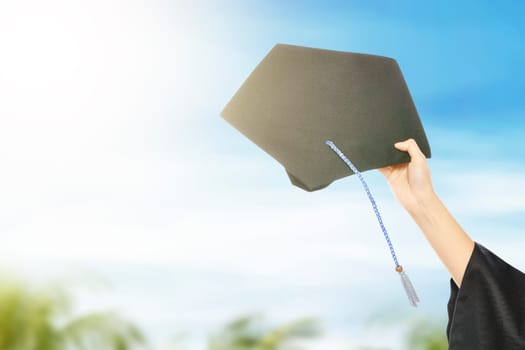 Hand holding graduation hat with blue sky background. Graduation concept