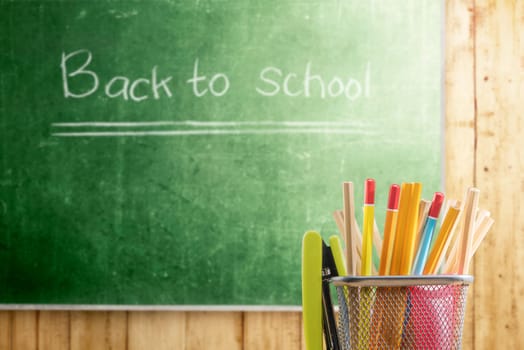 Pencils in basket container with green stapler with chalkboard background. Back to School concept