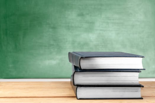 Pile of books on wooden table with chalkboard background. Back to School concept