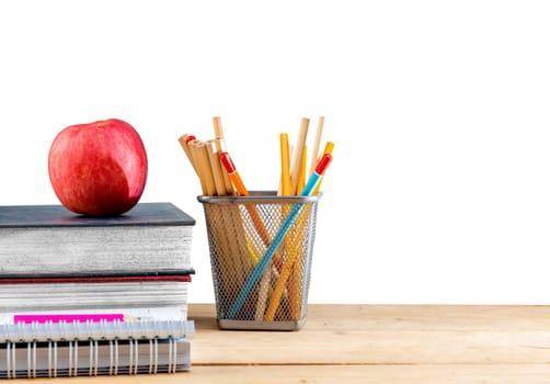 Pile of books with apple and pencils in basket container on wooden table isolated over white background. Back to School concept