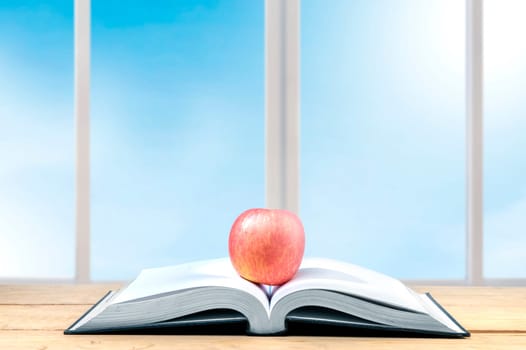 Apple on the middle of opened book on the wooden table. Back to School concept