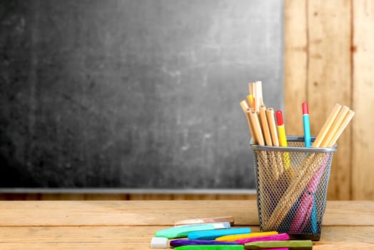 Pencils in basket container and colorful crayons on the wooden table with blackboard background. Back to School concept