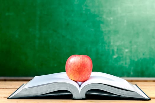 Apple on the middle of opened book on wooden table with chalkboard background. Back to School concept