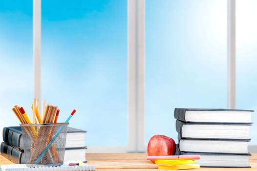 Pile of books with notes paper and pen, apple and pencils in basket container on the wooden table. Back to School concept