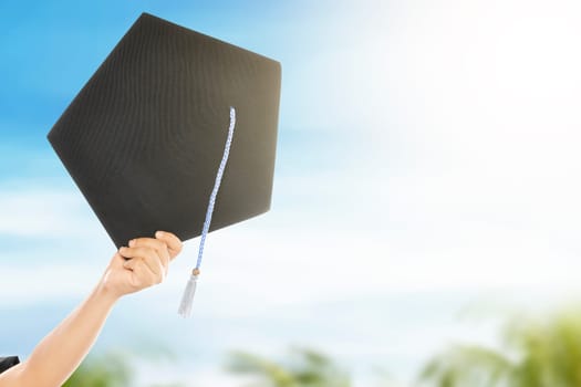 Hand holding graduation hat with blue sky background. Graduation concept