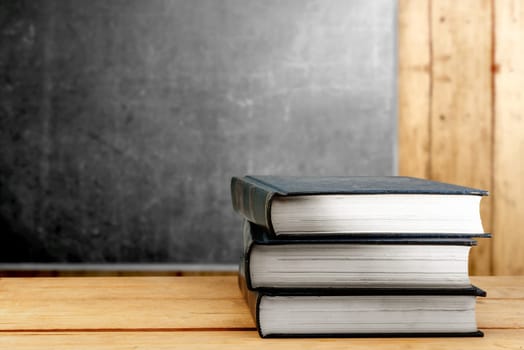 Pile of books on wooden table with blackboard background. Back to School concept