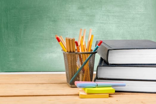 Pile of books with notes paper and pen with pencils in basket container on wooden table with chalkboard background. Back to School concept