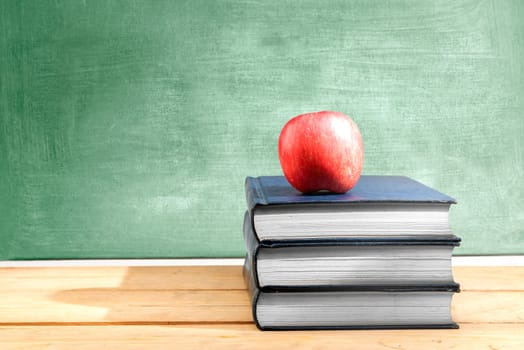 Pile of books with apple on the wooden table with chalkboard background. Back to School concept