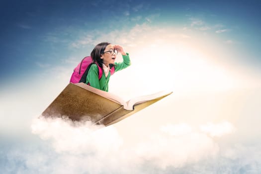 Asian cute girl with glasses and backpack sitting on the book with blue sky background. Back to School concept