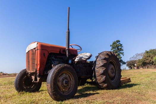 Old vintage tractor in farm field still operating with attached grass cutter.
