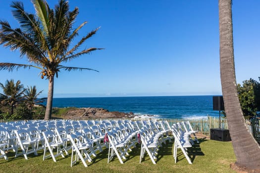 White Chairs dozens setting for Wedding Venue function home lawn front of beach blue ocean horizon summer landscape.