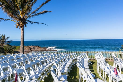 White Chairs dozens setting for Wedding Venue function home lawn front of beach blue ocean horizon summer landscape.