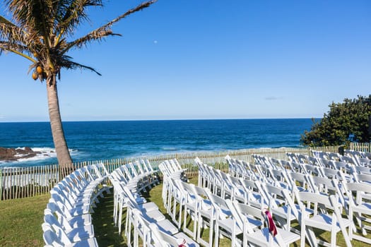 White Chairs dozens setting for Wedding Venue function home lawn front of beach blue ocean horizon summer landscape.