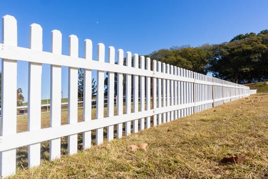 Boundary three feet wood white fence boundary across grass field blue sky day