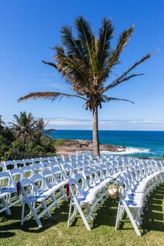 White Chairs dozens setting for Wedding Venue function home lawn front of beach blue ocean horizon summer landscape.