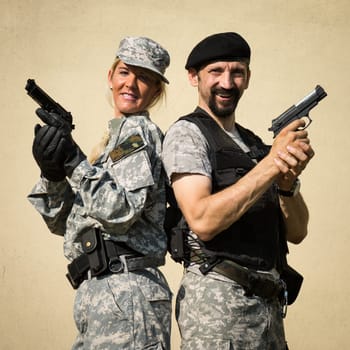 The smiling female and male soldiers in military uniform are posing with pistols in hands.