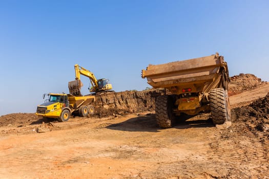 Construction industrial earthworks excavator machine loading earth soil into large truck vehicles.