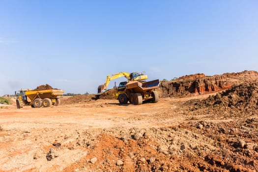 Construction industrial earthworks excavator machine loading earth soil into large truck vehicles.