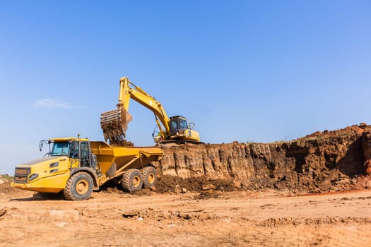 Construction industrial earthworks excavator machine loading earth soil into large truck vehicles.