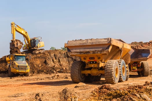 Construction industrial earthworks excavator machine loading earth soil into large truck vehicles.
