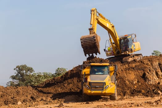 Construction industrial earthworks excavator machine loading earth soil into large truck vehicles.