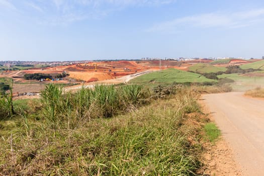 Industrial construction site overlooking large project expansion with graders,excavators,cranes machines into countryside sugarcane fields expanding earthworks infrastructure.