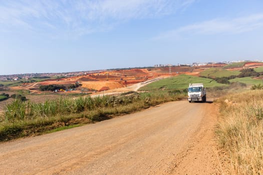 Industrial construction site overlooking large project expansion with graders,excavators,cranes machines into countryside sugarcane fields expanding earthworks infrastructure.