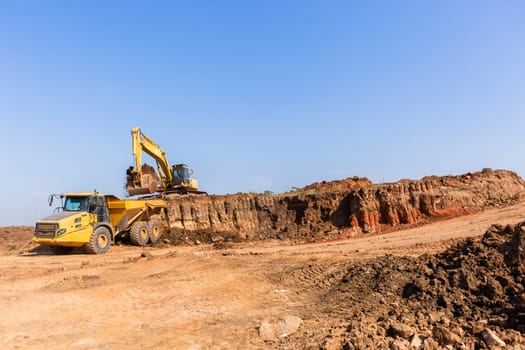 Construction industrial earthworks excavator machine loading earth soil into large truck vehicles.