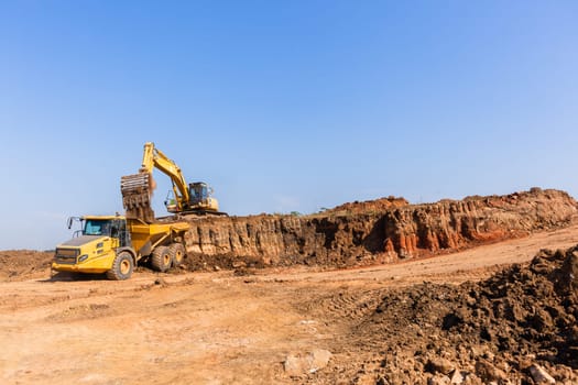 Construction industrial earthworks excavator machine loading earth soil into large truck vehicles.