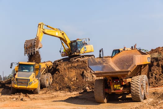 Construction industrial earthworks excavator machine loading earth soil into large truck vehicles.