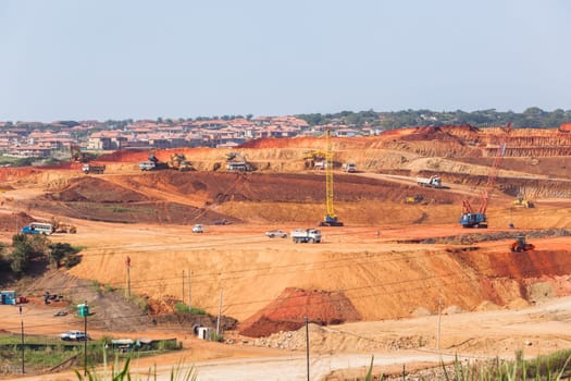 Industrial construction site overlooking large project expansion with graders,excavators,cranes machines into countryside sugarcane fields expanding earthworks infrastructure.