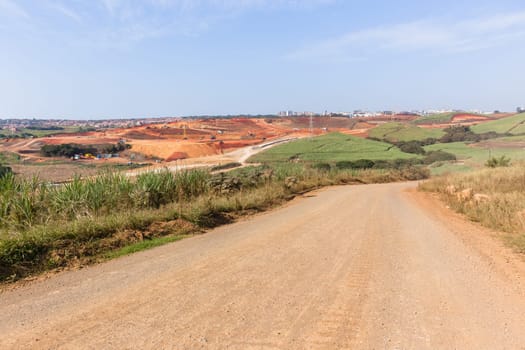 Industrial construction site overlooking large project expansion with graders,excavators,cranes machines into countryside sugarcane fields expanding earthworks infrastructure.