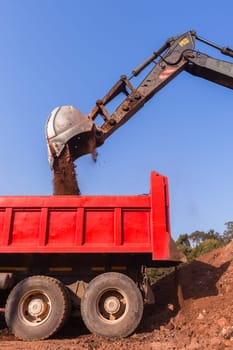 Construction industrial earthworks excavator machine loading earth soil into large truck vehicles.