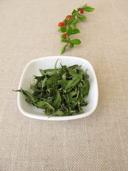 Dried goji leaves in a bowl and a fresh wolfberry twig