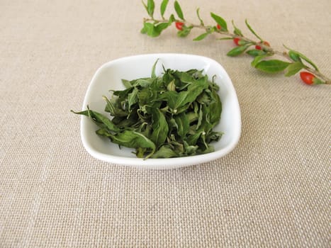 Dried goji leaves in a bowl and a fresh wolfberry twig