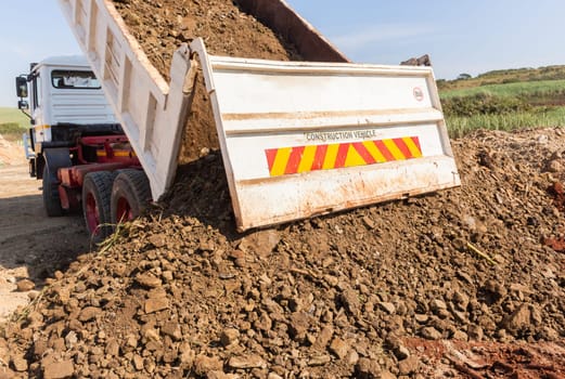 Construction Truck vehicle bucket bin tipping offloading earth closeup rear photo.