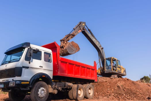 Construction industrial earthworks excavator machine loading earth soil into large truck vehicles.