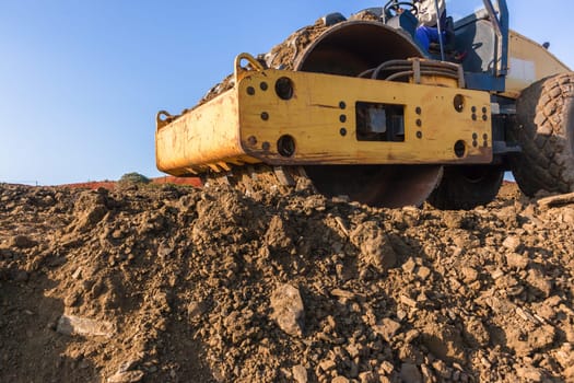 Construction industrial earthworks landfill compactor machine vibration leveling sand stones closeup abstract.